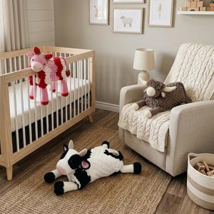 Può includere: Una scena di cameretta con una culla di legno e un giocattolo a forma di mucca all'uncinetto rosa, rosso e bianco. Un giocattolo a forma di mucca delle Highlands all'uncinetto marrone poggia su una coperta color crema in una poltrona beige. Un giocattolo a forma di mucca all'uncinetto bianco e nero è su un tappeto di iuta.