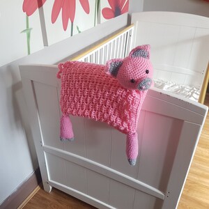 K&ouml;nnte beinhalten: Ein rosa geh&auml;keltes Schweinchenspielzeug mit grauen Ohren und Schnauze, das an einem wei&szlig;en Babybett h&auml;ngt.