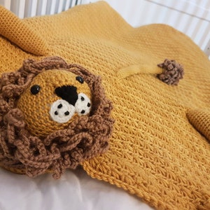 May include: A crocheted lion blanket in a mustard yellow color with a brown crocheted lion face and a tail.