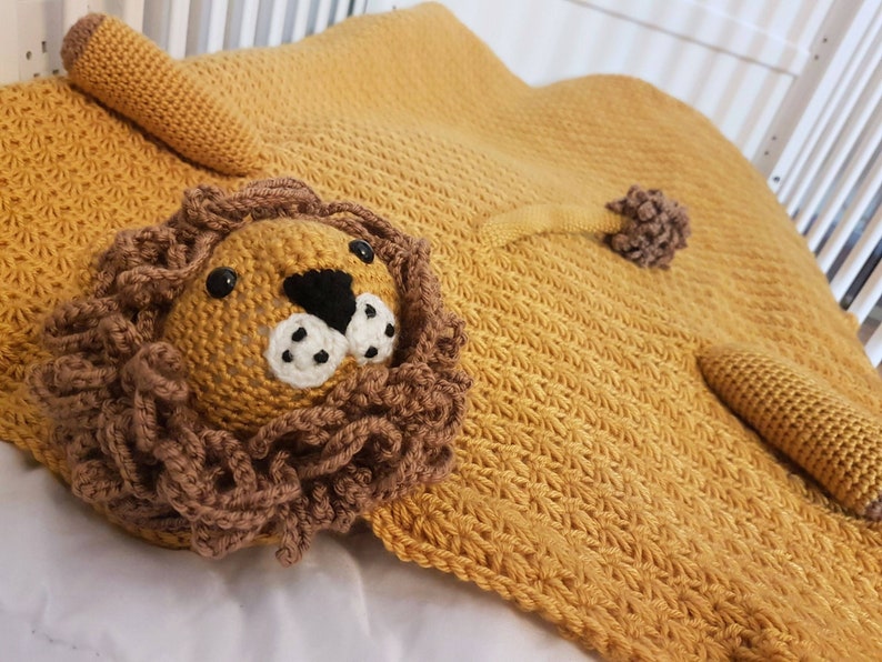 May include: A crocheted lion blanket in a mustard yellow color with a brown crocheted lion face and a tail.