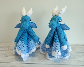 Könnte beinhalten: Zwei gehäkelte blaue Babydecken in Form von Drachen mit weißen Akzenten. Die Drachen haben weiße Hörner und Flügel. Die Decken sind aus hellblauem und weißem Garn gefertigt.