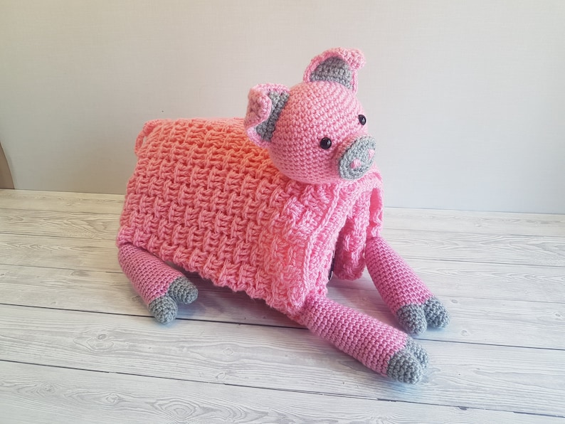 May include: A pink crocheted pig toy with grey accents. The pig is lying on its side with its legs outstretched. Pattern by Crafting Happiness