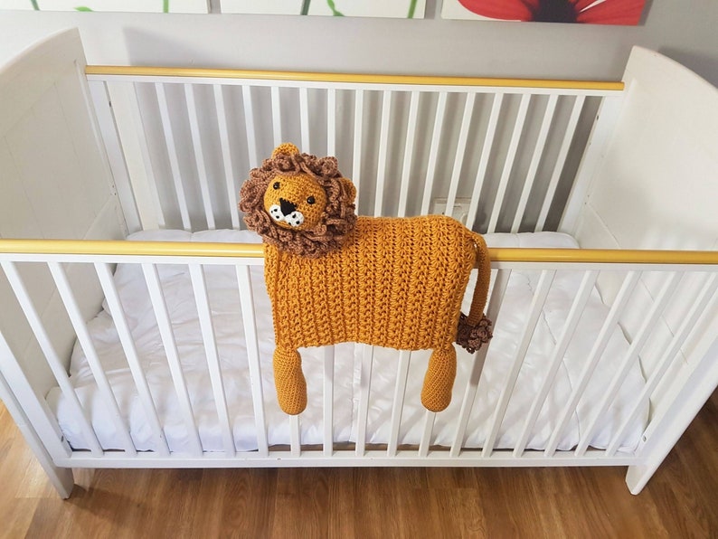May include: A crocheted lion toy with a brown mane and a white face, hanging over the side of a white crib.