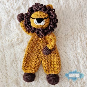 May include: A crocheted lion stuffed animal with brown and gold yarn. The lion has a brown mane, closed eyes, and a white nose. The lion is wearing a brown and gold crocheted outfit.