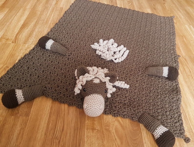 K&ouml;nnte beinhalten: Eine braune geh&auml;kelte Pferdedecke mit einem braunen geh&auml;kelten Pferdekopf und einer M&auml;hne. Die Decke hat einen braunen geh&auml;kelten Schwanz und vier Beine.