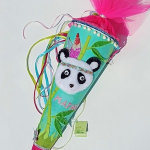 Könnte beinhalten: Ein türkisfarbener und grüner Schultüte mit einem Pandagesicht, Bambus und Federn. Die Tüte ist mit Glitzer verziert und hat oben eine rosa Tüllschleife. Die Tüte steht "Mafa" auf der Seite.