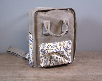 Könnte beinhalten: Grauer, rechteckiger Rucksack mit einer gemusterten Tasche mit Hasen, Blumen und Vögeln. Der Rucksack hat einen oberen Griff, einen verstellbaren Schultergurt und Seitentaschen. Geeignet für den täglichen Gebrauch.