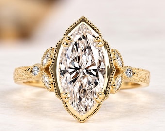 Puede incluir: Un anillo de oro amarillo con una gran piedra central de talla marquesa sujeta por garras en un engaste con borde milgrain. La banda está adornada con pequeñas piedras redondas y grabados detallados en forma de hoja en los laterales.