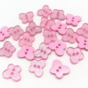 Könnte beinhalten: Eine Sammlung von rosa glitzernden Knöpfen in Blumenform mit jeweils zwei Löchern.