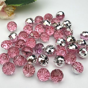 Könnte beinhalten: Eine Sammlung von facettierten Knöpfen in Pink und Silber. Die Knöpfe sind rund und haben eine glänzende Oberfläche.