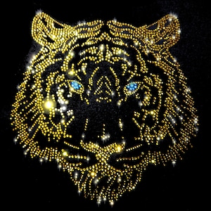 Op de afbeelding: Een gouden tijgergezichtsontwerp gemaakt van strass op een zwarte achtergrond. De ogen van de tijger zijn blauw.