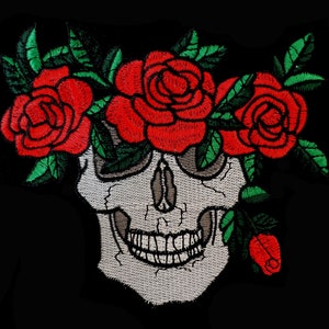 Könnte beinhalten: Gestickter Aufnäher mit einem weißen Totenkopf, der von einer Krone aus roten Rosen und grünen Blättern umgeben ist.