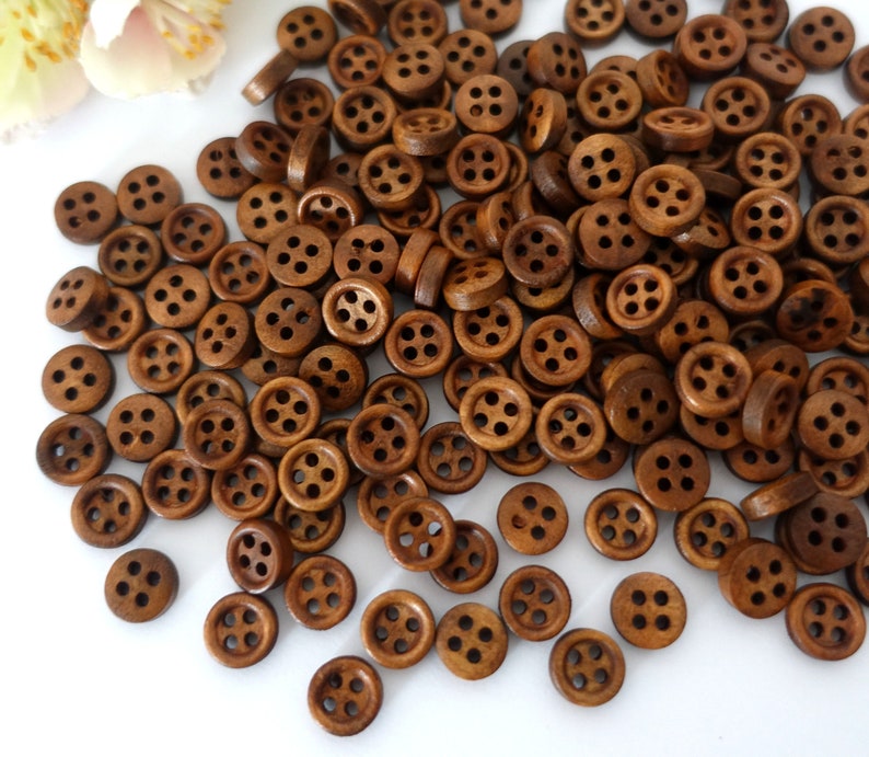 May include: A large pile of brown wooden buttons with four holes each. The buttons are scattered on a white surface.