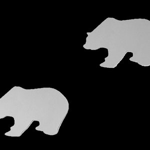 Op de afbeelding: Twee witte silhouet-uitsnijdingen van beren, die naar tegenovergestelde richtingen kijken, op een zwarte achtergrond.