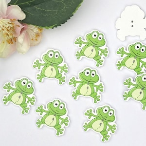 Könnte beinhalten: Acht grüne, holzschildförmige Knöpfe in Form eines Frosches mit weißen Umrissen und schwarzen Augen. Die Knöpfe haben eine genähte Linie in der Mitte des Froschkörpers.