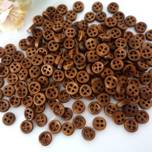 May include: A large pile of brown wooden buttons with four holes each. The buttons are scattered on a white surface.