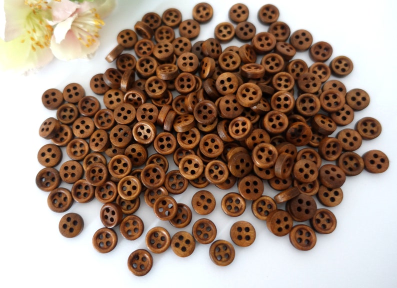 May include: A large pile of brown wooden buttons with four holes each. The buttons are scattered on a white surface.