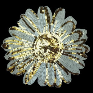 Peut inclure: Une applique de fleur en sequins dorés et blancs. La fleur a un grand centre et de nombreuses pétales.