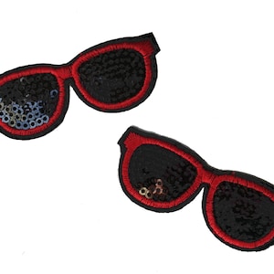 Puede incluir: Dos parches de gafas de sol de lentejuelas negras y rojas. Las gafas de sol tienen un contorno rojo y lentejuelas negras.