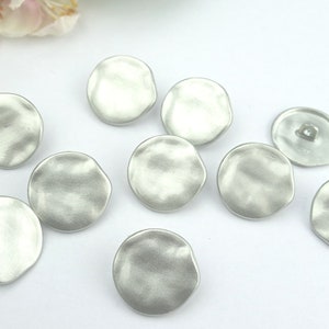 Peut inclure: Dix boutons ronds de couleur argentée avec une surface légèrement texturée. Les boutons mesurent environ 2,5 cm de diamètre.