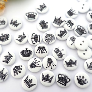May include: A collection of white wooden buttons with black crown designs. The buttons are round and have a smooth finish.