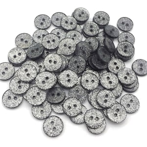 Może przedstawiać: Stos czarnych guzików z srebrnym brokatem. Guziki mają po dwa otwory.