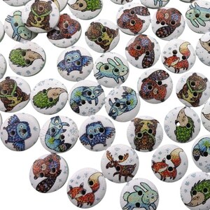 Könnte beinhalten: Sortiment aus Holz-Knöpfen mit verschiedenen Tiermotiven, darunter Eulen, Waschbären, Füchse und Hirsche. Die Knöpfe sind weiß mit glitzerndem Finish und zeigen farbenfrohe Tierillustrationen.
