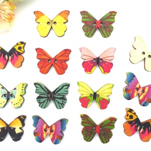Könnte beinhalten: Eine Sammlung von Holzknöpfen in Schmetterlingsform in verschiedenen Farben. Die Knöpfe weisen detaillierte Flügelmuster in Gelb-, Orange-, Rot-, Grün-, Rosa- und Lilatönen auf. Jeder Knopf hat zwei Löcher zum Annähen, vor weißem Hintergrund.