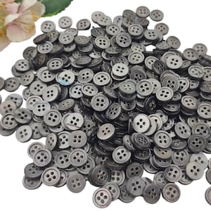 Peut inclure: Un grand tas de boutons gris à quatre trous. Les boutons sont faits d'un matériau lisse et brillant.