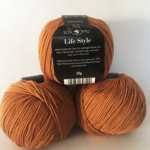 Könnte beinhalten: Drei Knäuel braunes Superwash-Merinowolle, beschriftet mit "Life Style" und dem Markennamen "Schoppel". Das Etikett lautet außerdem "Ideales Superwash Garn für vielseitigen Einsatz. Aus feiner Merinowolle. Extrafine virgin woolsuper wash yarn in fine count. 100% Schurwolle (Merino fine, superwash) 100% Virgin Wool/Laine/Lana/Lana/U/Villa/Voina/Gyap-jú/Vina/la/ull/Wol 50g"