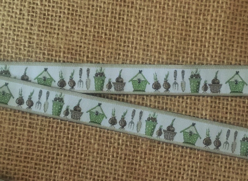 May include: White ribbon with a repeating pattern of green pots, brown bulbs, and small birdhouses. The ribbon has a light beige background.