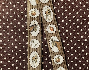 May include: Two strips of decorative ribbon with a repeating pattern of donkeys, pumpkins, and wheat stalks in oval frames. The ribbon has a tan background with a brown border and is set against a brown polka dot background.