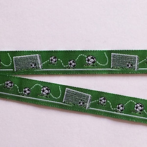 Könnte beinhalten: Grünes Band mit einem Fußballfeld-Design, das Fußbälle und Tore zeigt. Das Band hat ein sich wiederholendes Muster aus Fußbällen, Toren und Feldlinien. Das Band ist etwa 2,5 cm breit.