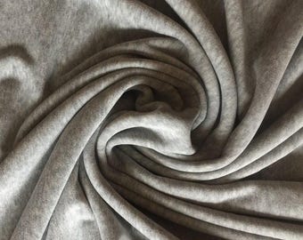 Puede incluir: Una tela gris claro suave con una textura jaspeada sutil, dispuesta en un patrón drapeado y giratorio. El material presenta pliegues profundos y sombras que resaltan la superficie lisa y mate, así como el color neutro y uniforme.