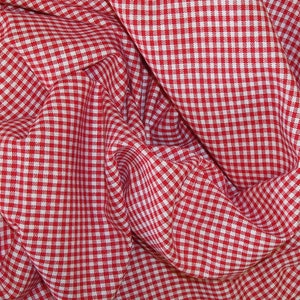Puede incluir: Tela de vichy roja y blanca con un patr&oacute;n a cuadros. La tela est&aacute; doblada y arrugada, creando un aspecto texturizado.