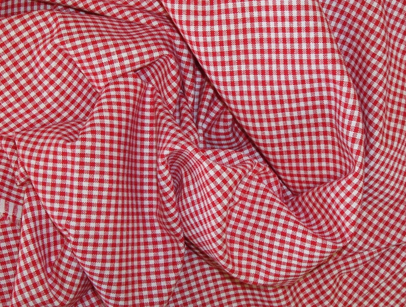 Puede incluir: Tela de vichy roja y blanca con un patr&oacute;n a cuadros. La tela est&aacute; doblada y arrugada, creando un aspecto texturizado.