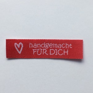 Könnte beinhalten: Rotes Stofflabel mit weißem Text "handgemacht FUR DICH" und einem weißen Herz.