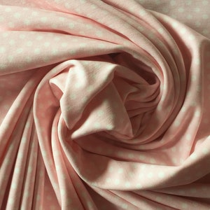 May include: Pink fabric with a white polka dot pattern. The fabric is folded and draped, showing the texture and softness of the material.