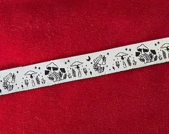 Puede incluir: Cinta blanca con un patrón negro repetido de setas, plantas, lunas y estrellas. La cinta está colocada sobre un fondo rojo.