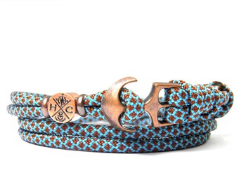 May include: A brown and blue paracord bracelet with a copper anchor charm and a copper compass charm with the letters "H" and "C" inside.