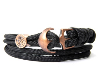 May include: Black paracord bracelet with a copper anchor charm and a copper bead with an engraved compass and the letters "H&C".
