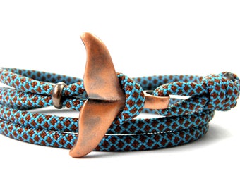 May include: A brown and blue braided rope bracelet with a copper whale tail charm.