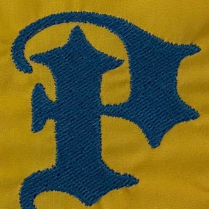 May include: A mustard yellow fabric background featuring a large, dark blue embroidered letter P in a gothic, old English style font. The embroidery has a visible, textured stitch pattern that stands out against the smooth yellow textile.