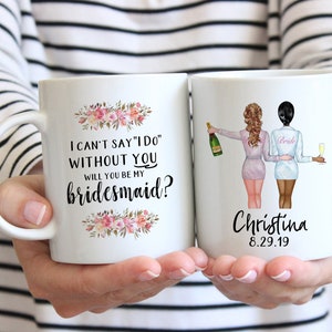 Puede incluir: Dos tazas de café blancas con texto negro y diseños florales. Una taza dice "No puedo decir "Sí, quiero" sin ti. ¿Quieres ser mi dama de honor?" La otra taza tiene un dibujo de dos mujeres con batas, una sosteniendo una botella de champán y la otra sosteniendo una copa de champán. El texto en la segunda taza dice "Christina 8.29.19".