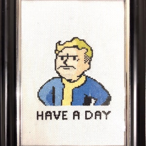 May include: Cross-stitch embroidery of a cartoon character with blonde hair wearing a blue jacket and a yellow shirt. The text "HAVE A DAY" is below the character.