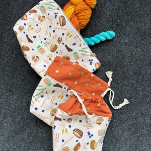 May include: A collection of fabric pouches and yarn. The pouches feature a bread-themed pattern with text. Orange and yellow yarn and a small turquoise skein are also present. The pouches are in various sizes and shapes.