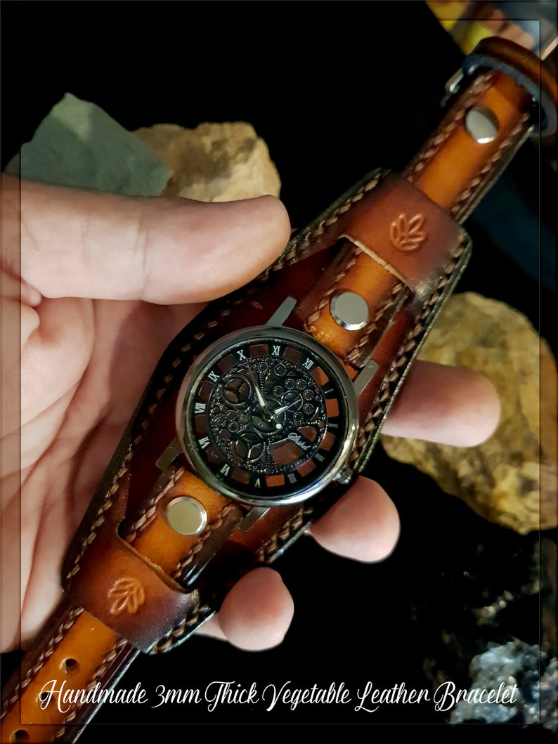 May include: A brown leather watch band with a silver watch face. The watch face has a black background with silver Roman numerals and a skeletonized design. The band is 3mm thick and is made of vegetable tanned leather. Handmade 3mm Thick Vegetable Leather Bracelet.