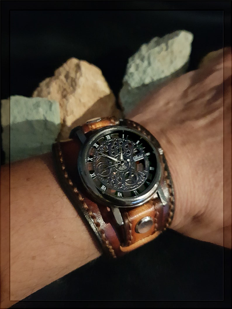 May include: A brown leather watch band with a silver watch face featuring a skeletonized movement. The watch face has Roman numeral hour markers and a black background.