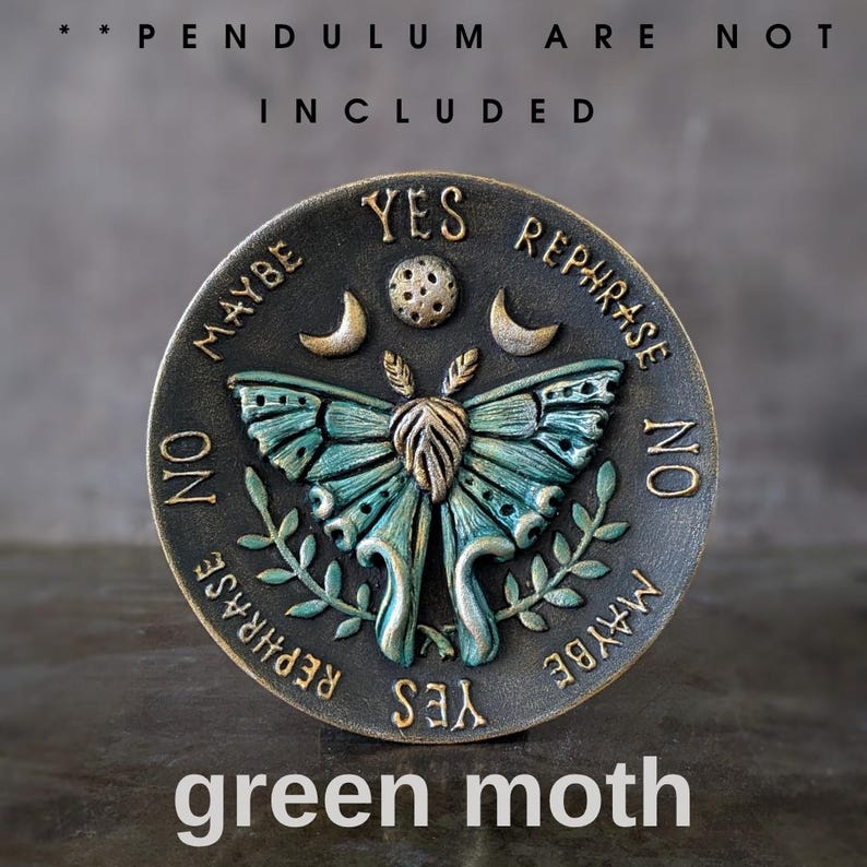 May include: A circular bronze-toned divination board featuring a central teal and gold moth, flanked by crescent moons and a dotted circle. The text reads YES, NO, MAYBE, and REPHRASE around the perimeter. Text at the top states PENDULUM ARE NOT INCLUDED.