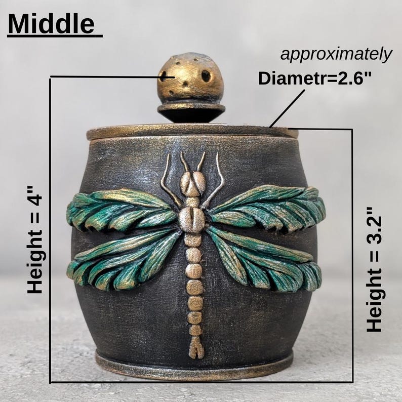 May include: A dark gray and gold lidded jar featuring a sculpted dragonfly with green wings. The jar has a height of 4 inches, a body height of 3.2 inches, and a lid diameter of 2.6 inches. The text Middle is visible at the top left corner.